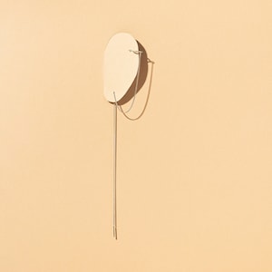 Könnte beinhalten: Eine silberne Kettenkette mit einer zarten Kette und einem kleinen Anhänger, der vor einem beigefarbenen Hintergrund hängt.