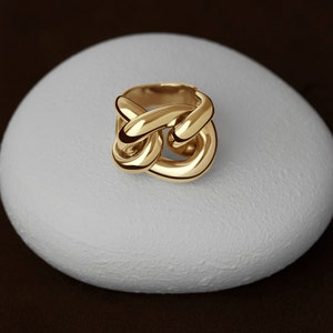 May include: A gold ring with a knot design. The ring is on a white stone surface.