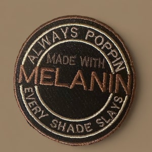 May include: A brown and white embroidered patch with the text "Always Poppin Made With Melanin Every Shade Slays".