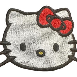 May include: A white embroidered iron-on patch of Hello Kitty with a red bow.