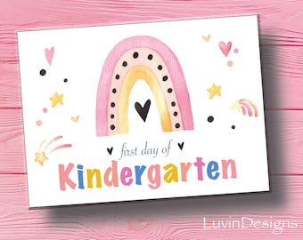 May include: A pink, yellow, and white watercolor rainbow with black polka dots and a black heart in the center. The text "first day of kindergarten" is written in colorful letters below the rainbow. There are stars, hearts, and shooting stars scattered around the rainbow.