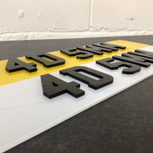 May include: Black acrylic numbers 4D 5MM on a white and yellow background. The numbers are raised and have a glossy finish.