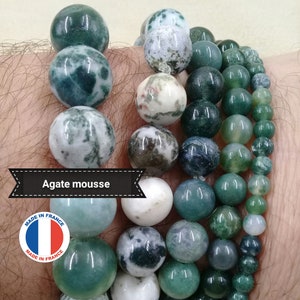 Peut inclure: Un ensemble de quatre bracelets en agate mousse verte et blanche. Les bracelets sont empilés sur le poignet d'une personne. Les bracelets sont étiquetés "Agate mousse" et "Fabriqué en France".