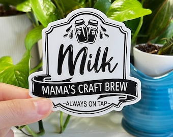 May include: White sticker with black text and illustrations. The sticker says "Milk Mama's Craft Brew -Always on Tap-." The sticker has two illustrations of milk bottles with a drip of milk coming from each.