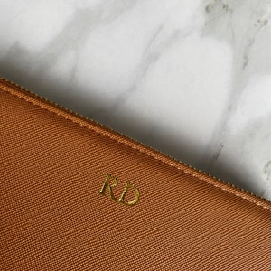 K&ouml;nnte beinhalten: Eine braune Leder-Rei&szlig;verschlusstasche mit goldenen Initialen "RD" auf der Vorderseite.