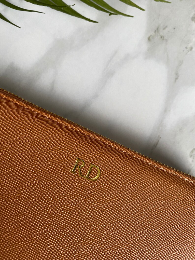 K&ouml;nnte beinhalten: Eine braune Leder-Rei&szlig;verschlusstasche mit goldenen Initialen "RD" auf der Vorderseite.