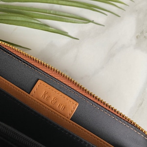 K&ouml;nnte beinhalten: Das Innere einer braunen Leder-Rei&szlig;verschlusstasche mit schwarzem Stofffutter. Die Tasche hat ein braunes Lederetikett mit dem gepr&auml;gten Text "KE & CO".