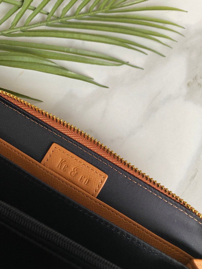 K&ouml;nnte beinhalten: Das Innere einer braunen Leder-Rei&szlig;verschlusstasche mit schwarzem Stofffutter. Die Tasche hat ein braunes Lederetikett mit dem gepr&auml;gten Text "KE & CO".