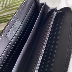 May include: Black leather zippered wallet with multiple compartments and a silver zipper pull.