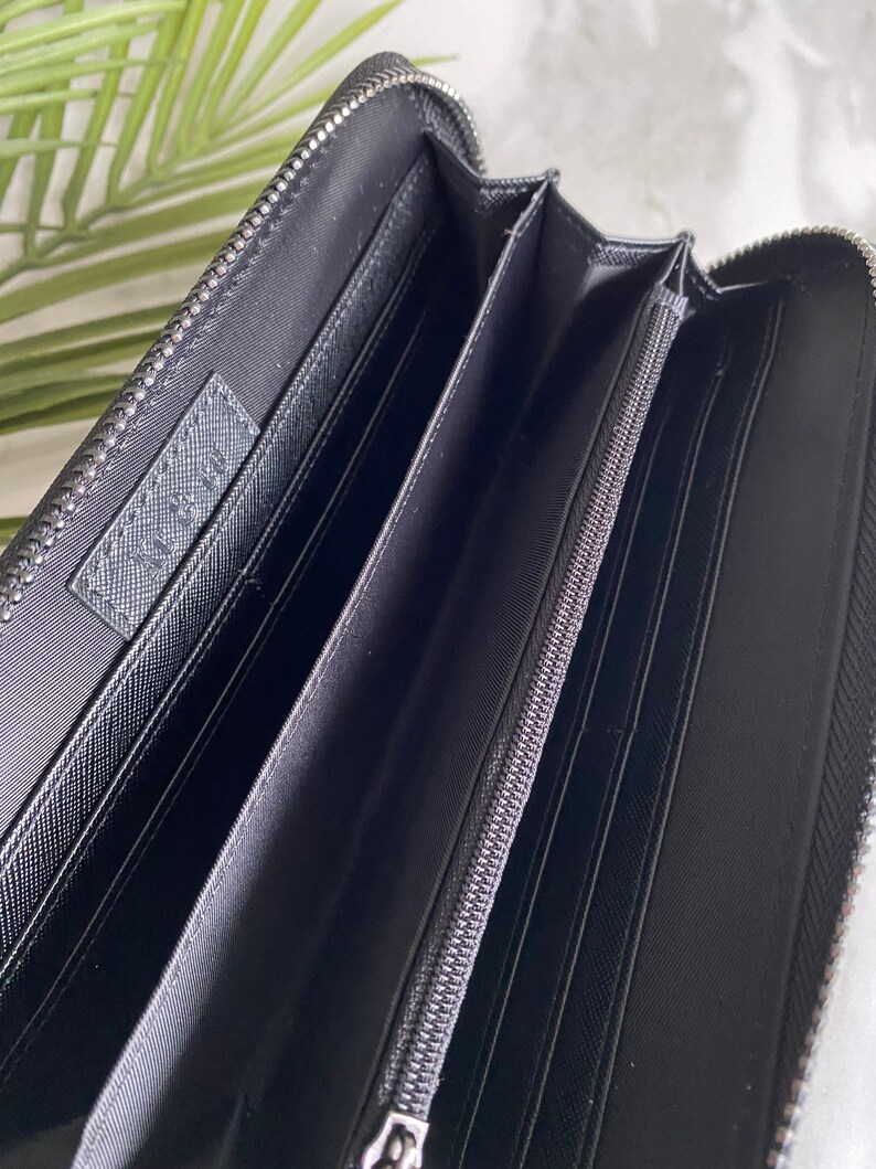 May include: Black leather zippered wallet with multiple compartments and a silver zipper pull.