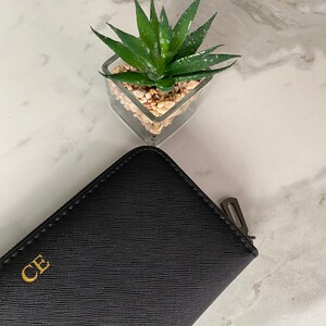 May include: A black leather wallet with a gold zipper and the initials "CE" embossed on the front.