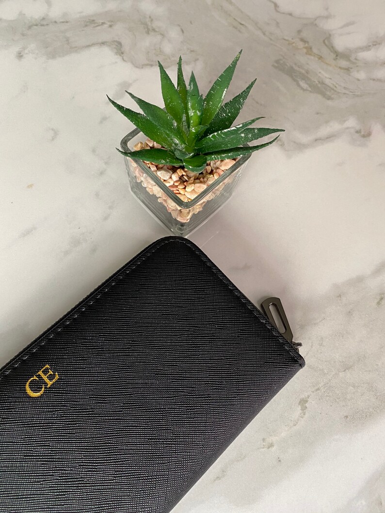 May include: A black leather wallet with a gold zipper and the initials "CE" embossed on the front.
