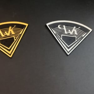 Könnte beinhalten: Zwei dreieckige Metallplaketten mit einem schwarzen und weißen Baseballstadion-Design. Die Plaketten sind golden und silberfarben.