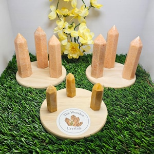 May include: Six orange crystal points on wooden stands, arranged in two groups of three. The stands are on a green grassy surface. A sticker with the text "The Wooden Crystals" is on one of the stands.