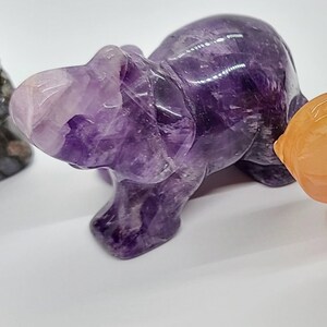 May include: A small, purple amethyst elephant figurine. The elephant is carved from a single piece of amethyst and has a smooth, polished finish.