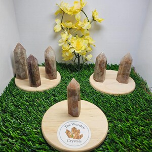 May include: Five brown and white striped crystal points on wooden bases with a green grass background. The bases have a sticker that says "The Wooden Crystals".