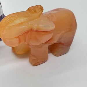May include: A small, orange-colored, carved stone elephant figurine. The elephant has a smooth, polished surface and is standing on all four legs.