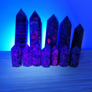 May include: A collection of eight purple and black crystal points, arranged in a row on a wooden surface. The crystals are all pointed and have a rough, natural texture.