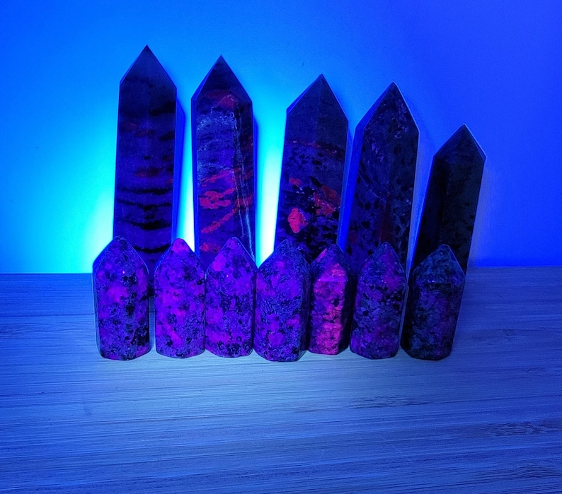 May include: A collection of eight purple and black crystal points, arranged in a row on a wooden surface. The crystals are all pointed and have a rough, natural texture.