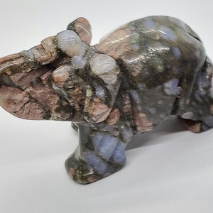 May include: A small, hand-carved elephant figurine made of pink, gray, and blue speckled stone. The elephant is standing with its trunk raised.