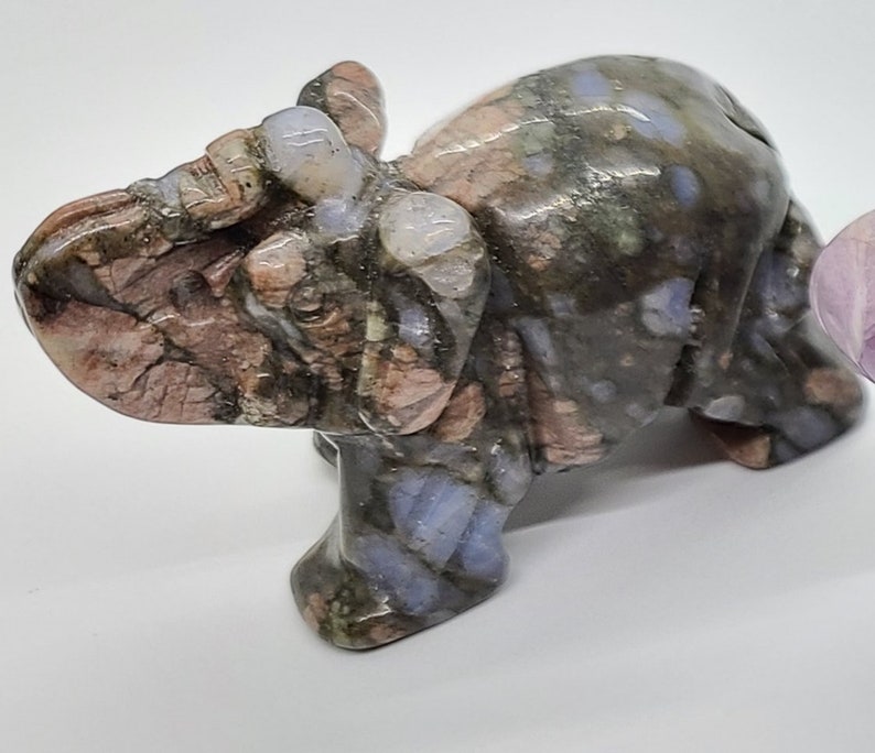 May include: A small, hand-carved elephant figurine made of pink, gray, and blue speckled stone. The elephant is standing with its trunk raised.