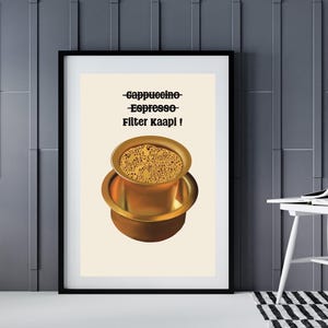 May include: Framed print featuring a golden coffee filter with coffee grounds. The print has the words "-Cappuccino- Espresso- Filter Kaapi !" in black text. The background is a light beige color.