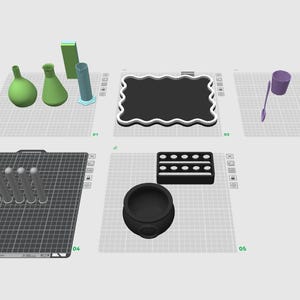 May include: A digital 3D modeling interface displaying various objects on five separate grid platforms, including green laboratory glassware, a black scalloped tray, purple cups, a spoon, five gray cylinders, a black rectangular tray, and a cauldron.
