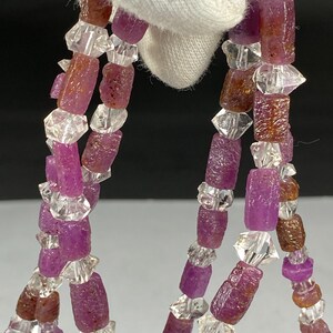 May include: A strand of pink and clear gemstone beads. The beads are faceted and have a rough, natural look. The beads are strung on a clear thread.