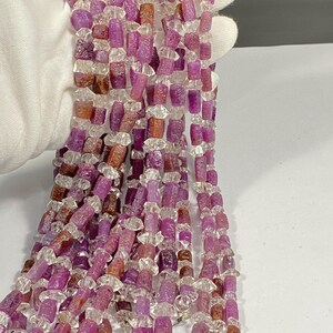 Può includere: Una collana di perline di pietra preziosa sfaccettate rosa e trasparenti. Le perline sono di forma irregolare e hanno una superficie ruvida e testurizzata.