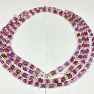 Può includere: Una collana multifilo realizzata con perline di pietre preziose sfaccettate rosa e trasparenti. La collana è composta da tre fili di perline, ognuno con un motivo diverso. Le perline sono tutte della stessa dimensione e forma, e sono infilate su una catena d'argento.