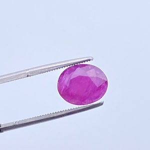 May include: A round, pink gemstone with a faceted cut. The gemstone is held by a pair of tweezers.