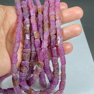 May include: A strand of pink and brown faceted gemstone beads. The beads are rectangular in shape and have a rough, natural texture.
