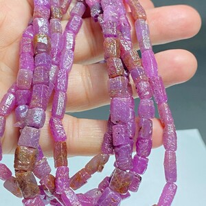 May include: A strand of pink ruby beads, each bead is faceted and has a rectangular shape. The beads are strung on a clear thread and are approximately 10mm in length.