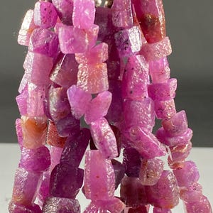 May include: A strand of pink ruby gemstone beads, each bead is faceted and has a unique shape. The beads are strung on silver wire.