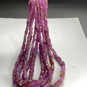May include: A strand of pink ruby beads, each bead is a rectangular shape with a rough, faceted surface. The beads are strung on a silver wire and are ready to be used for jewelry making.
