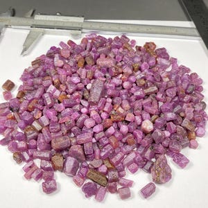 Puede incluir: Un montón grande de piedras preciosas de rubí rosa en bruto. Las piedras en bruto son de varios tamaños y formas.