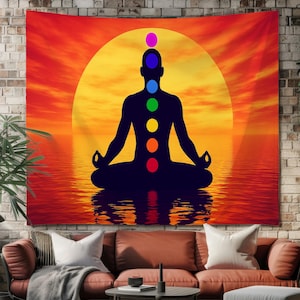 Può includere: Un arazzo da parete che mostra la sagoma scura di una persona in posizione di meditazione seduta su uno sfondo di un vibrante tramonto arancione e giallo. Sette simboli circolari colorati dei chakra sono allineati verticalmente.