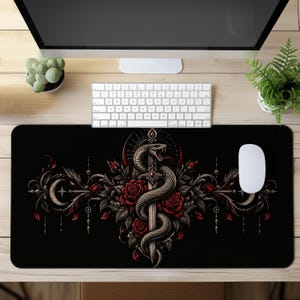 Può includere: Un tappetino da scrivania rettangolare nero con una grafica centrale raffigurante un serpente avvolto attorno a una spada verticale, circondato da rose rosso scuro, fogliame scuro e motivi a mezzaluna, con elementi decorativi simmetrici.