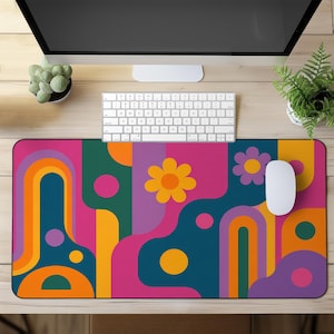 May include: A brightly coloured desk mat with a retro floral design. The mat features a vibrant pattern of flowers, arches, and geometric shapes in shades of pink, orange, yellow, teal, and purple. A white computer mouse and keyboard are on the mat.