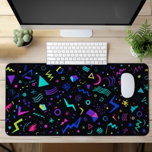 Puede incluir: Una alfombrilla de escritorio rectangular con fondo negro y un patrón repetitivo de formas geométricas de colores neón, incluyendo triángulos, zigzags, círculos y rayos en tonos rosa, azul, verde y amarillo sobre la superficie.