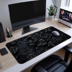 May include: Black and white floral design mouse mat with a black computer mouse on top. The mouse mat is on a black desk with a computer monitor and a potted plant.