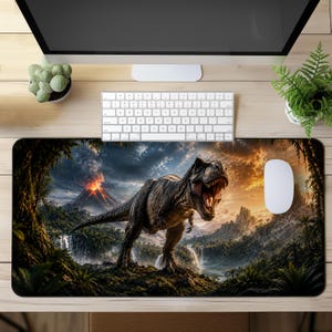 May include: A rectangular desk mat featuring a detailed illustration of a Tyrannosaurus Rex standing in a prehistoric landscape. The scene includes a volcanic eruption with smoke, lush green jungle foliage, waterfalls, and a sunset sky.