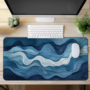 Puede incluir: Un tapete de ratón con un diseño abstracto de olas azules y blancas. El tapete de ratón está sobre un escritorio de madera con una computadora, un teclado y plantas en macetas.