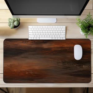 May include: A rectangular desk mat featuring a dark, abstract, painterly design with blended shades of deep brown, rust orange, and black. The surface has a textured, weathered appearance with horizontal strokes, providing a wide area for a computer mouse.