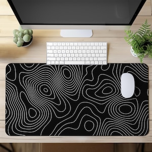 Könnte beinhalten: Schwarzes Mauspad mit weißem topografischem Design. Das Pad hat ein sich wiederholendes Muster aus weißen Konturlinien auf schwarzem Hintergrund. Eine weiße Maus und Tastatur liegen auf dem Holzschreibtisch.