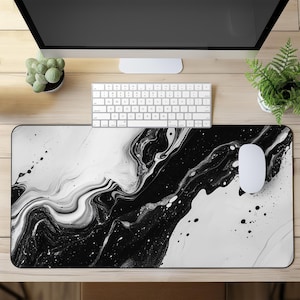 Puede incluir: Alfombrilla de ratón con diseño abstracto en blanco y negro. El diseño presenta un patrón similar al mármol con remolinos y salpicaduras. Un ratón blanco está a la derecha, y un teclado blanco está encima.