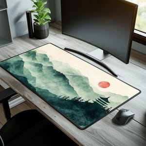 Könnte beinhalten: Eine große, rechteckige Mausmatte mit einem grünen und weißen Aquarelldesign von Bergen und einer roten Sonne. Die Mausmatte liegt auf einem Holztisch mit einem Computermonitor und einer Topfpflanze.