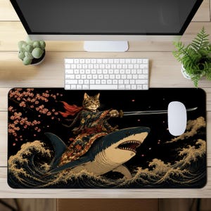 Puede incluir: Una alfombrilla de escritorio rectangular con una ilustración gráfica de un gato atigrado vestido con ropa tradicional japonesa, empuñando una katana mientras monta un tiburón a través de olas estilizadas y ramas de cerezo sobre un fondo negro.