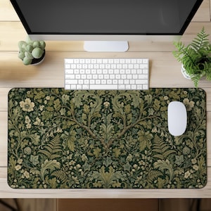 May include: A rectangular desk mat featuring a dark green background with a dense, symmetrical botanical pattern of light green oak leaves, ferns, and small white flowers. The mat is positioned on a wooden desk surface beneath a computer monitor.