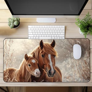 May include: A brown and white horse and a brown and white foal stand in a snowy field. The horse is looking at the camera, while the foal is looking to the side. The background is a snowy field with trees in the distance.